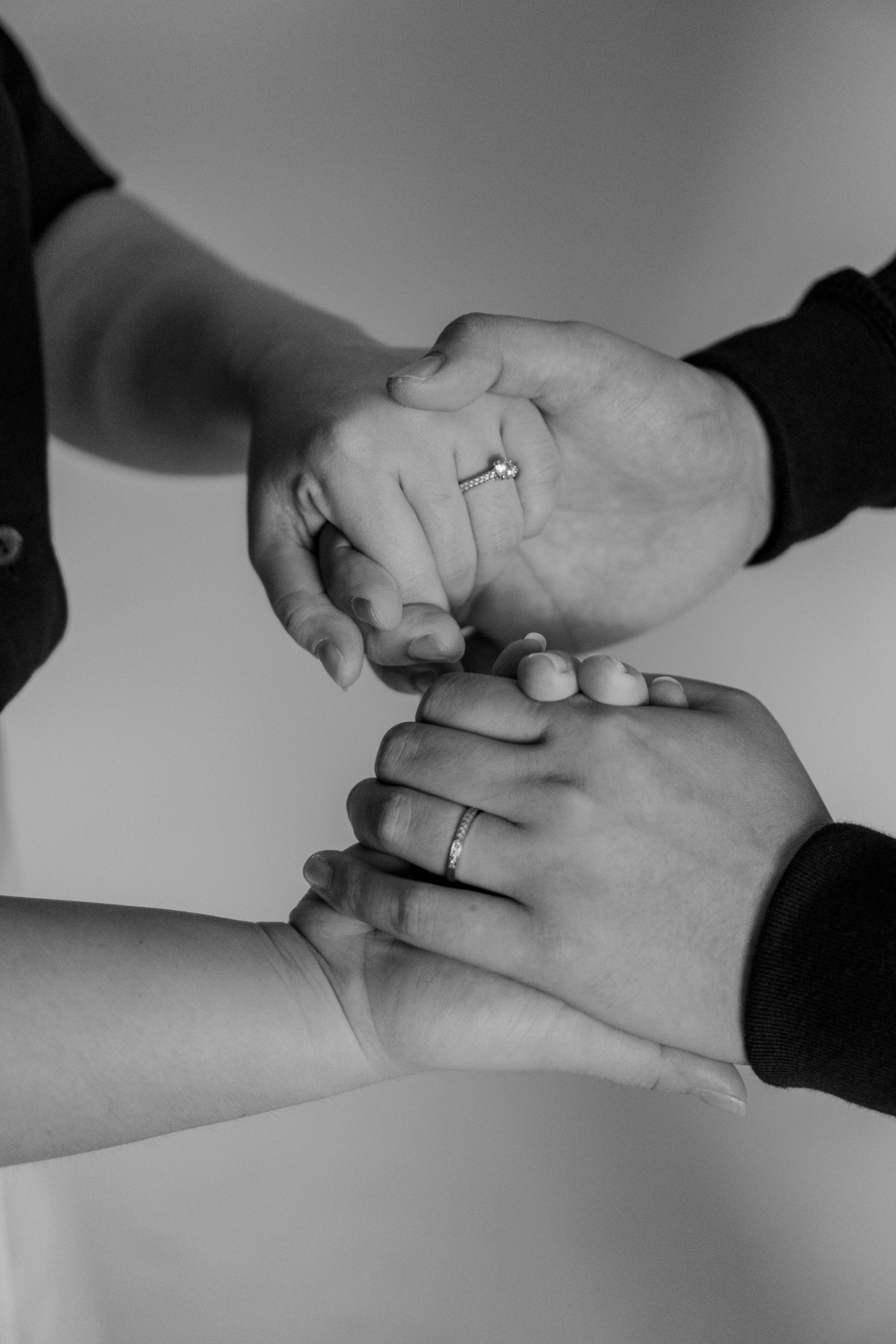 Black-and-white close-up of two people holding hands, both wearing rings